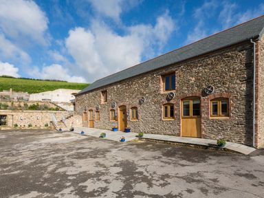 An exterior view of a stone building with multiple wooden doors and windows and flower pots outside at Butterwell Barn Dartmouth