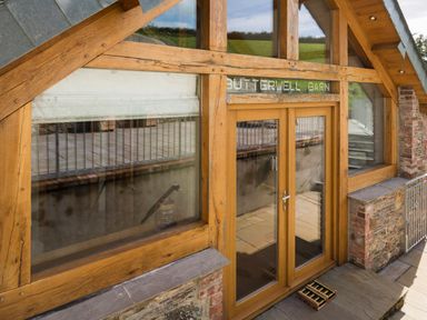 Exterior wooden framed glass doors and windows of a building with stone and brick walls at Butterwell Barn in Dartmouth