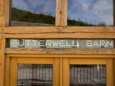 A wooden door with glass panels and a stained glass sign above reading Butterwell Barn at Butterwell Barn in Dartmouth
