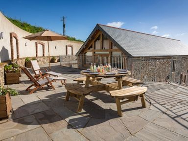 An outdoor patio with wooden picnic table set with plates and drinks and two reclining chairs with umbrella at Butterwell Barn in Dartmouth