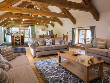 An open living and dining room with wooden beams and sofas around a coffee table at Butterwell Barn in Dartmouth