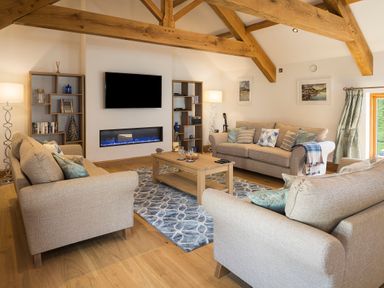 A living room with three beige sofas a wooden coffee table a wall-mounted television and wooden beams at Butterwell Barn in Dartmouth