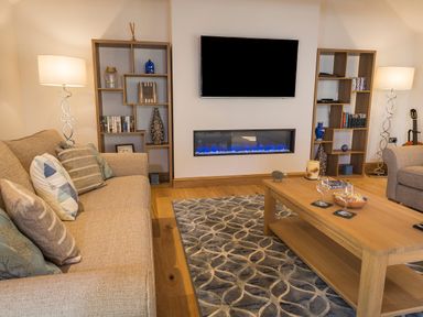 A living room with beige sofas a wooden coffee table two floor lamps and a wall mounted television at Butterwell Barn in Dartmouth