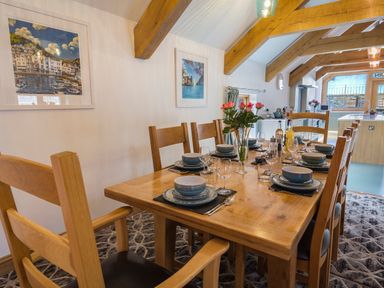 A dining table set with plates glasses and a flower vase in a room with wooden beams at Butterwell Barn in Dartmouth