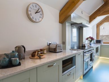 A kitchen with a clock on the wall tea set bread and jars on the counter stove and wooden beams at Butterwell Barn in Dartmouth