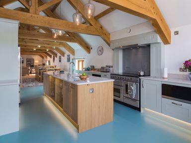 A kitchen with wooden beams a central island with sink a large stove and blue floor at Butterwell Barn in Dartmouth