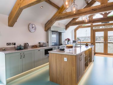 A kitchen with wooden beams, an island counter, appliances, a clock on the wall, and glass doors at Butterwell Barn in Dartmouth
