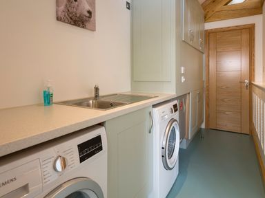 A utility room with washing machines a sink cupboards and a wooden door at Butterwell Barn in Dartmouth