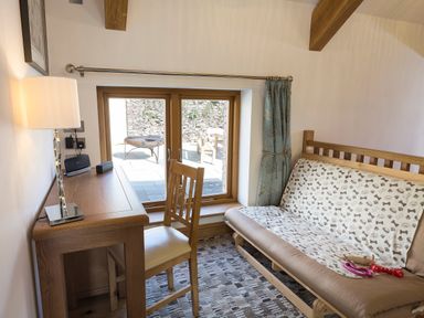 A small room with a wooden desk and chair beside a window and a sofa bed covered with a patterned throw at Butterwell Barn in Dartmouth