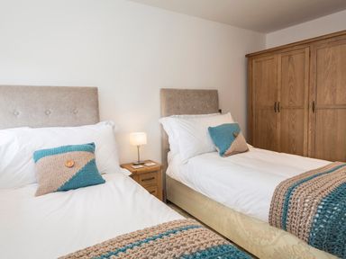 A bedroom with two single beds bedside table with lamp and wooden wardrobe at Butterwell Barn in Dartmouth