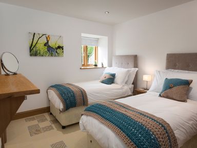A bedroom with two single beds with knitted throws and cushions a wooden window and a wall painting of a hare at Butterwell Barn in Dartmouth