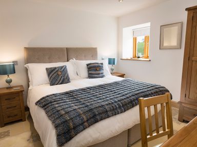 A bedroom with a double bed two bedside tables with lamps a wooden chair and a wooden wardrobe at Butterwell Barn in Dartmouth