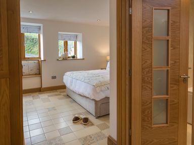 A bedroom with a bed slippers on tiled floor and two windows with patterned blinds at Butterwell Barn in Dartmouth