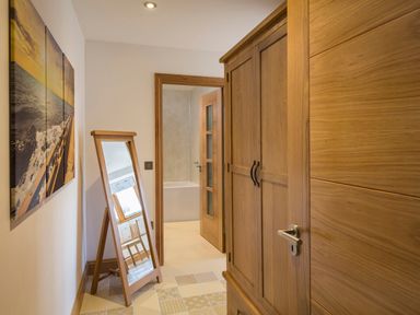 A hallway with a wooden wardrobe a standing mirror a painting on the wall and a door leading to a bathroom at Butterwell Barn in Dartmouth