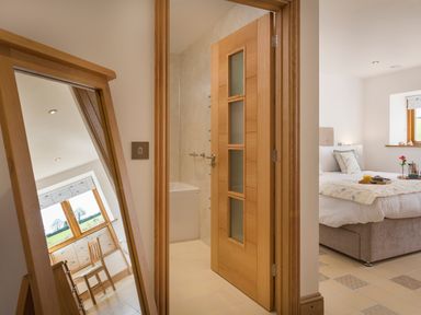 A bedroom with a bed and window next to a bathroom with an open wooden door and a mirror reflecting a chair at Butterwell Barn in Dartmouth
