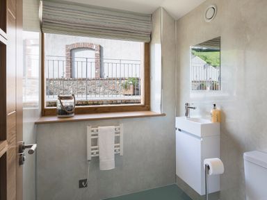 A bathroom with a window towel rail a small sink with a mirror and a toilet at Butterwell Barn Dartmouth