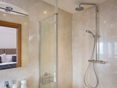 A bathroom with a shower area and a mirror reflecting part of a bedroom at Butterwell Barn in Dartmouth