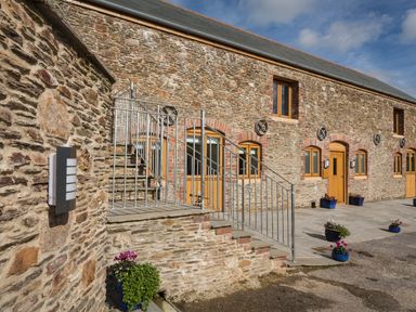 An exterior view of a stone building with wooden doors and windows a metal staircase and potted plants at Butterwell Barn in Dartmouth