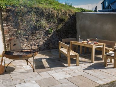 An outdoor patio with a metal barbecue grill and wooden table with benches set against stone and stucco walls at Butterwell Barn in Dartmouth