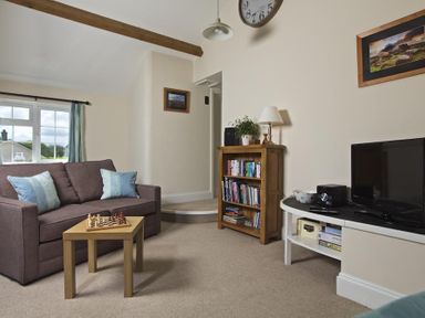 A living room with a sofa with pillows a small table with a chess set a wooden bookshelf and a TV on a white stand at Cloverwell in Woodleigh