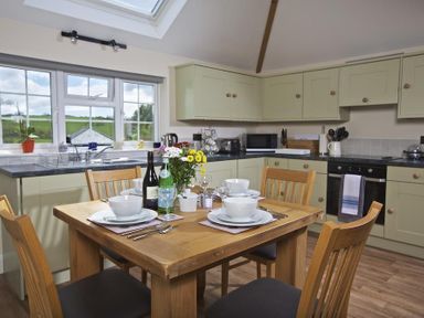 A kitchen with a wooden dining table set for four with dishes and flowers at Cloverwell in Woodleigh