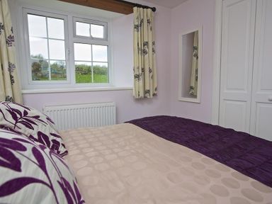 A bedroom with a bed near a window curtain a wall mirror and built in white wardrobes at Cloverwell in Woodleigh