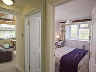 A hallway with doors leading to a bedroom with a bed and window and a living area with sofa and kitchen at Cloverwell in Woodleigh