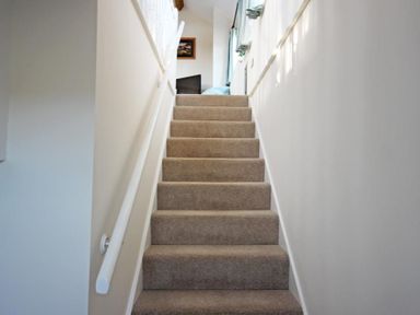 A carpeted staircase with white walls and handrails leading to a room with a television at Cloverwell in Woodleigh