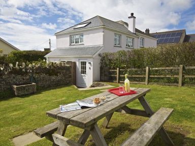A wooden picnic table on grass with drinks and snacks outside a two-story white house with a garden fence at Cloverwell in Woodleigh