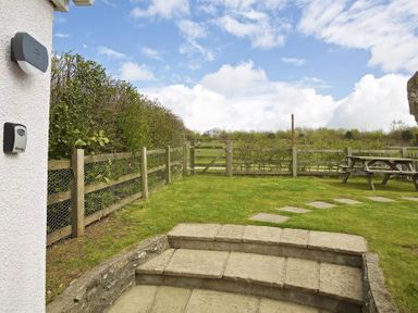 A garden with stone steps leading to a grassy area and wooden fence with a gate and picnic table at Cloverwell in Woodleigh