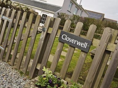 A wooden gate with a Cloverwell sign and a garden with grass and flowers at Cloverwell in Woodleigh