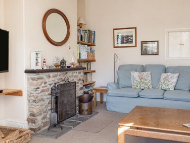 A living room with a stone fireplace sofa with floral cushions wooden coffee table and bookshelves at Cottage View in Hope Cove