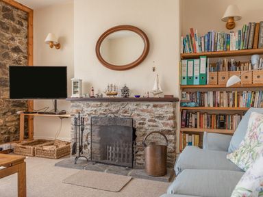A living room with a stone fireplace TV bookshelf and blue sofa at Cottage View in Hope Cove
