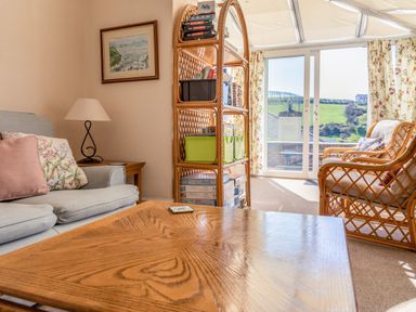 A living room with a coffee table sofa armchairs bookshelf and sliding glass doors at Cottage View in Hope Cove