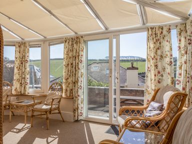 A sunroom with wicker chairs and glass tables with floral curtains and a sliding glass door at Cottage View in Hope Cove