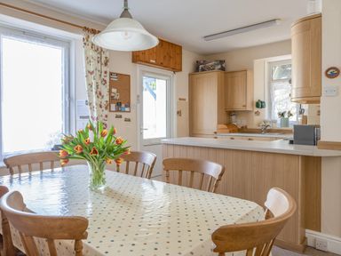 A kitchen with wooden chairs around a table with a vase of tulips at Cottage View in Hope Cove