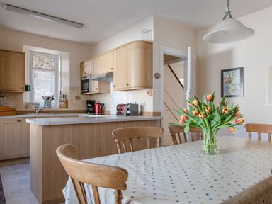 A kitchen with wooden cabinets a dining table with a vase of tulips and wooden chairs at Cottage View in Hope Cove