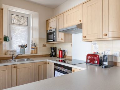 A kitchen with wooden cabinets a sink a microwave coffee maker kettle toaster and coffee machine at Cottage View in Hope Cove