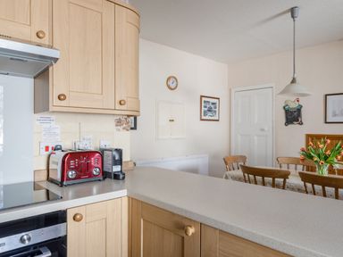A kitchen with wooden cabinets a red toaster a coffee machine and a dining table with tulips at Cottage View in Hope Cove