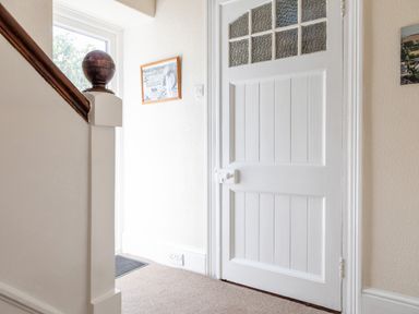 A hallway with a white paneled door and a wooden stair banister at Cottage View in Hope Cove