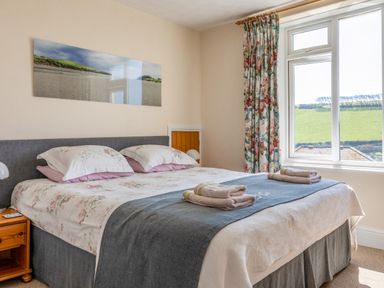 A bedroom with a double bed pillows towels bedside table and window with floral curtains at Cottage View in Hope Cove
