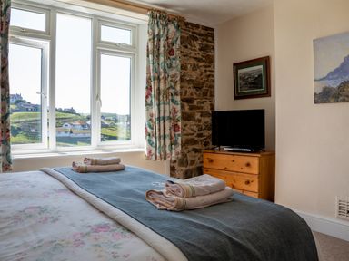A bedroom with a bed with folded towels on it a window with curtains and a wooden dresser with a television at Cottage View in Hope Cove