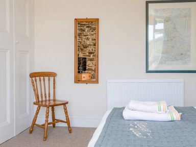 A bedroom corner with a wooden chair a wall-mounted mirror a map framed on the wall and towels on a bed at Cottage View in Hope Cove