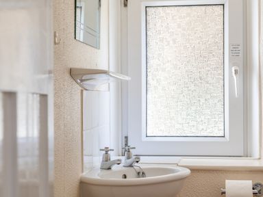 A bathroom sink with two taps under a frosted window at Cottage View in Hope Cove
