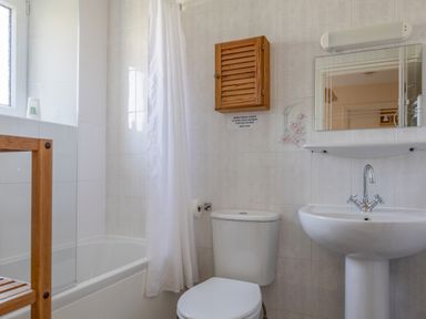A bathroom with a bathtub curtain a toilet a wooden shelf a wall cabinet a sink and a mirror at Cottage View Hope Cove