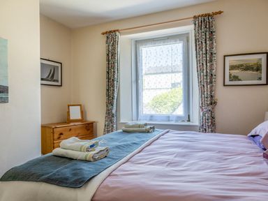 A bedroom with a bed towels on it a window with curtains a wooden chest of drawers and framed pictures on the wall at Cottage View in Hope Cove