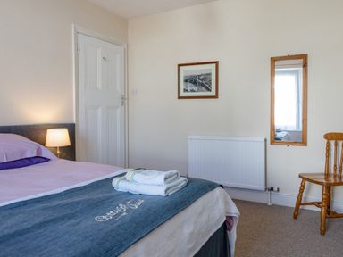A bedroom with a bed and towels on it a wooden chair a wall mirror and a framed picture at Cottage View in Hope Cove