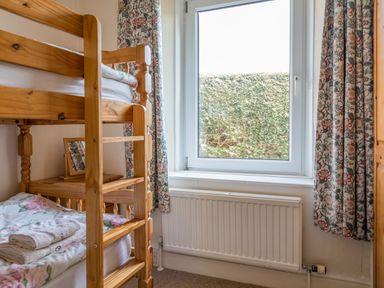 A bedroom with wooden bunk beds near a window with floral curtains and a radiator below at Cottage View in Hope Cove