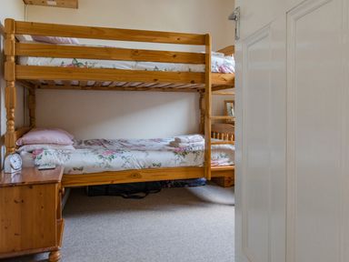 A bedroom with wooden bunk beds and a bedside table with a clock and remote at Cottage View Hope Cove