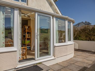 A patio door leading to a sunroom with rattan chairs and a bookshelf at Cottage View in Hope Cove